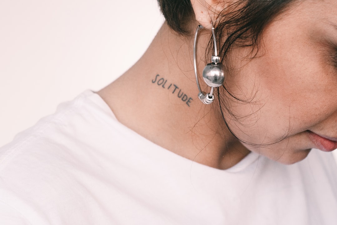 woman wearing white crew-neck shirt with solitude neck tattoo
