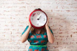 woman covering face using wall clock