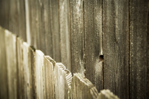 Weathered wooden fence panels with visible texture and natural aging, featuring a rustic and rugged appearance.