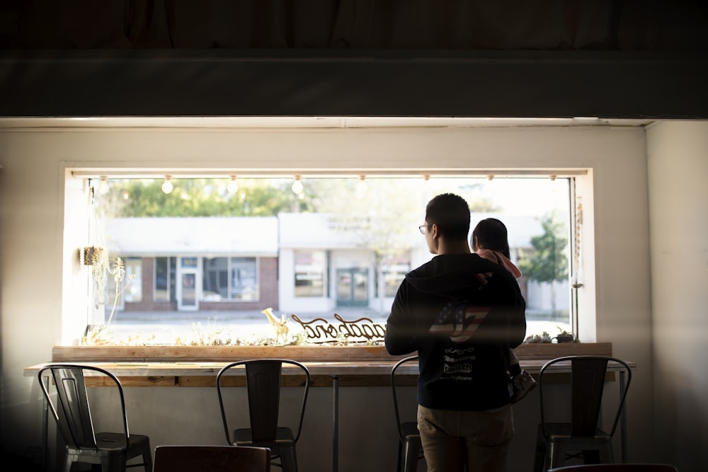 man carrying child looking through window during daytime