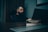 A man with a beard is sitting at a desk in a dimly lit office, looking at a laptop. The desk has a nameplate that reads 'I'M NOT BOSSY, I am the boss.' The atmosphere is calm and introspective.