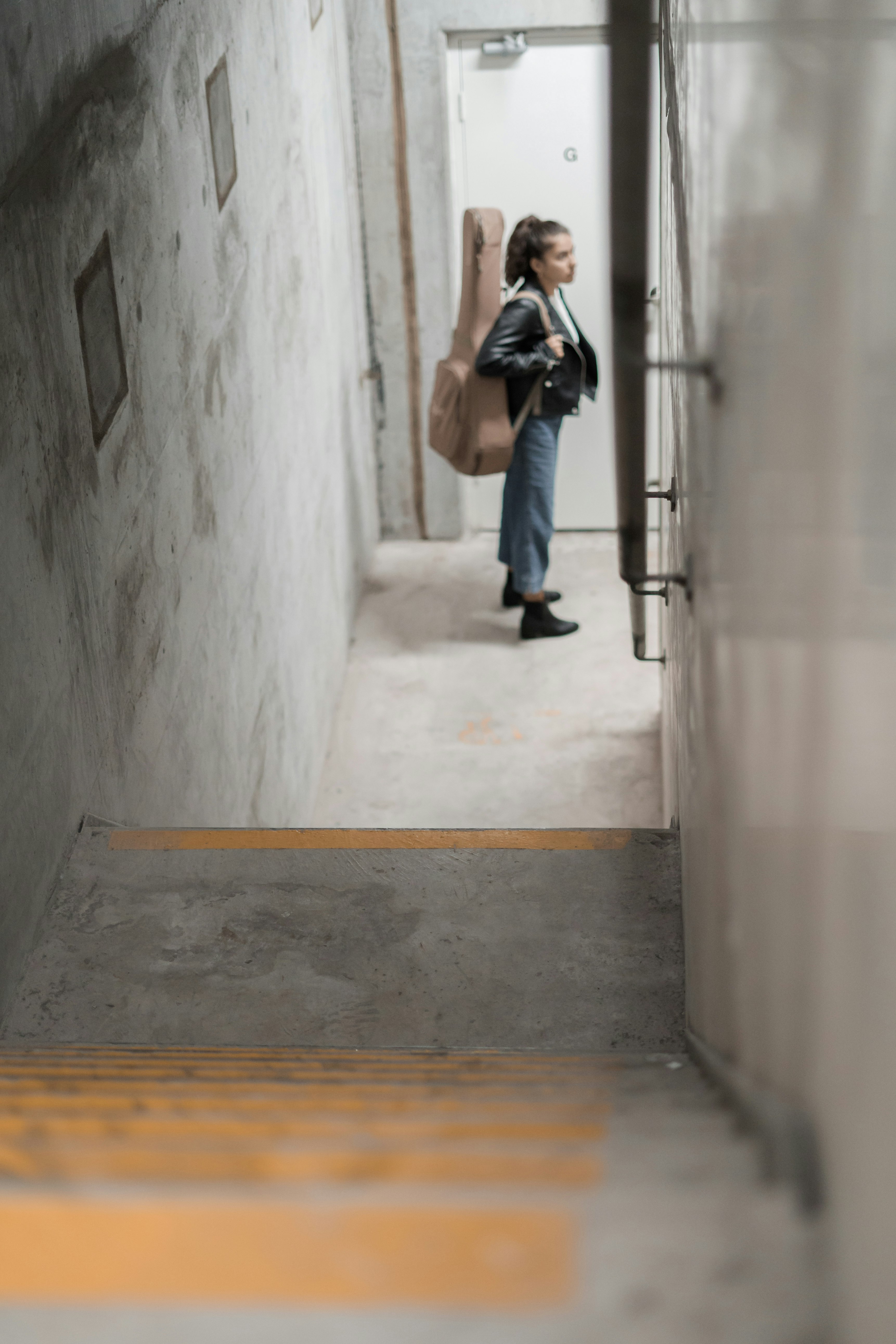 woman carrying brown acoustic guitar gig bag by the door