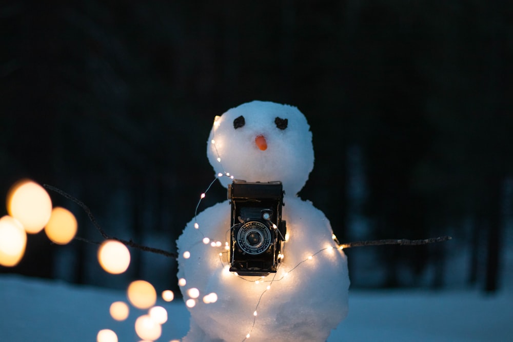 Schneemann mit beleuchteter Lichterkette und schwarzer DSLR-Kamera