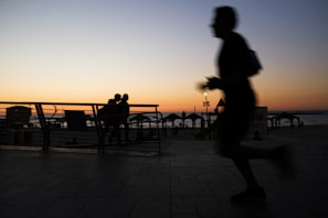 Silhouetted joggers pacing along the shoreline as dawn breaks over the sea