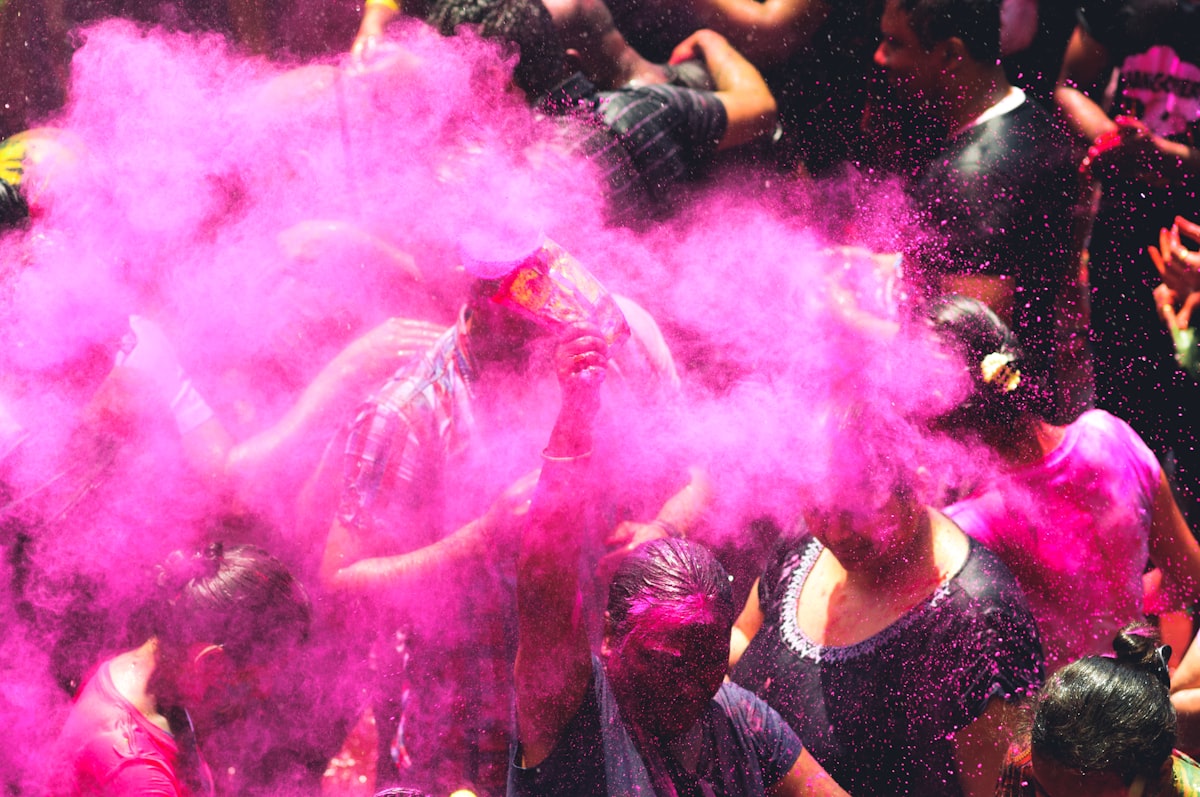 People celebrating Holi with clouds of purple and pink powder. Photo by Anshu A on Unsplash.