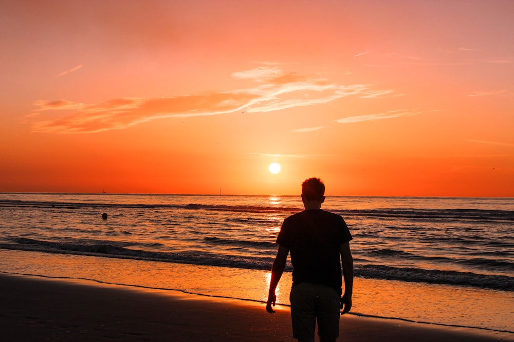 man standing near shore during sunset