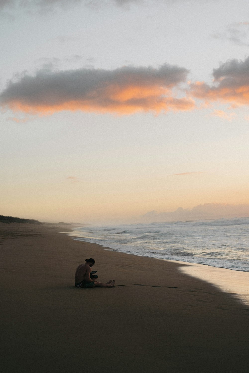 man sitting on seashore during sunset