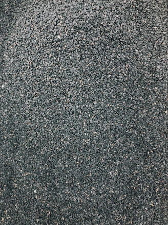 Close-up of vibrant pepper seeds spilling from a rustic wooden scoop onto rich soil.