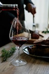 person pouring red wine on wine glass