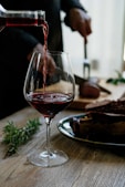 person pouring red wine on wine glass