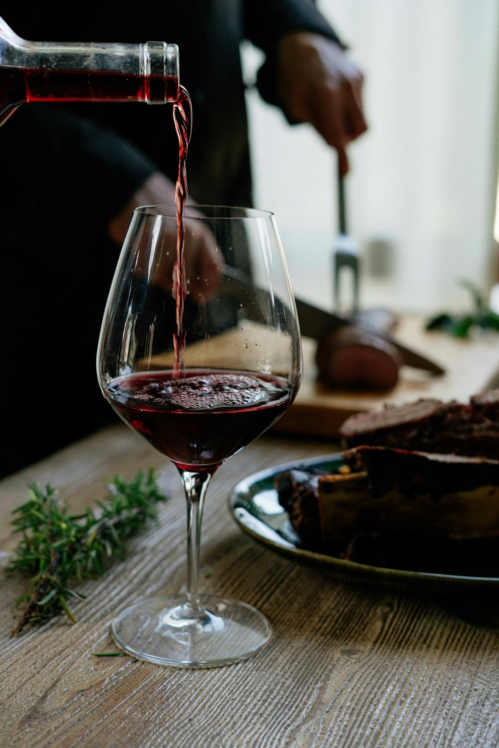 personne versant du vin rouge sur un verre à vin