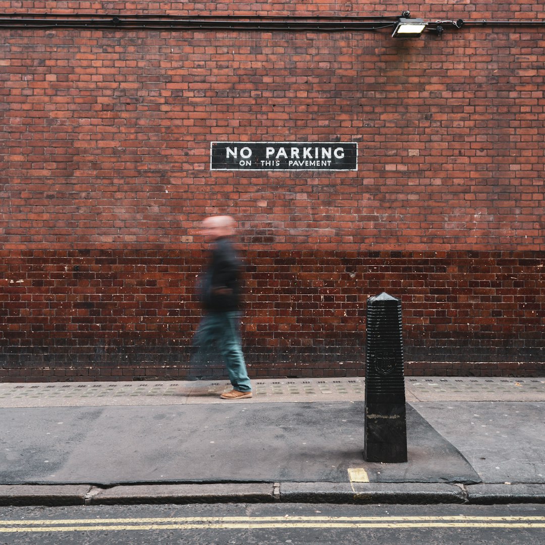 person walking near concrete wall with No Parking signage