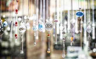 An array of intricately designed hanging pendants and necklaces featuring a variety of gemstones and ornate patterns. The pendants are displayed vertically, each showcasing unique designs like filigree work and colorful beads.