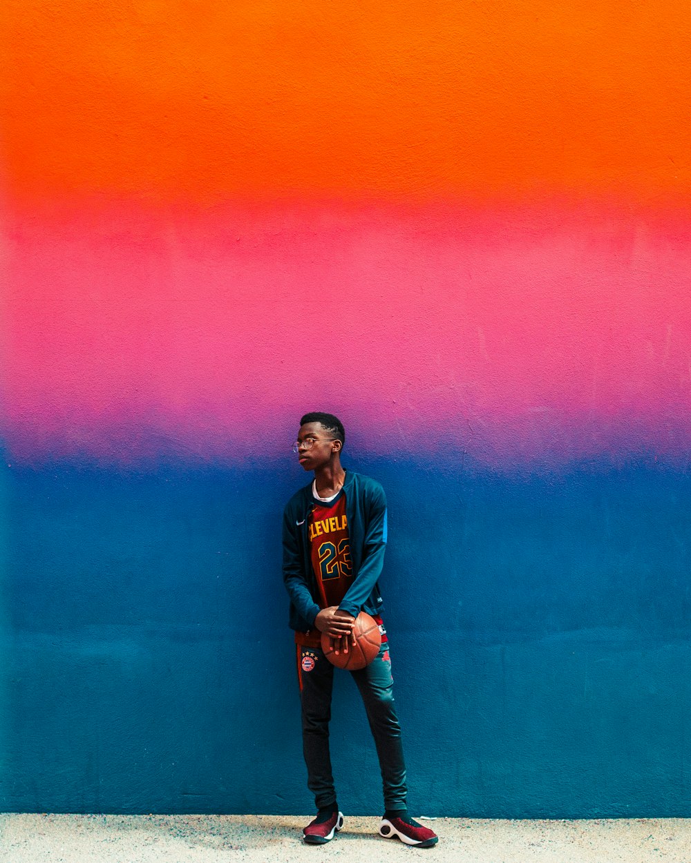 garçon debout et tenant un ballon de basket-ball à côté d’un mur peint en bleu et rose