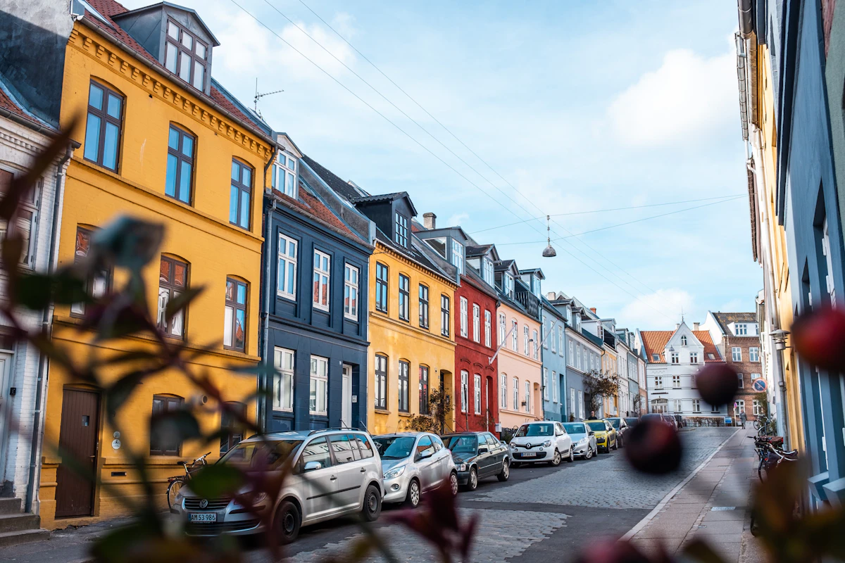 Gade i Aarhus C med farverige huse og parkerede biler en solrig dag