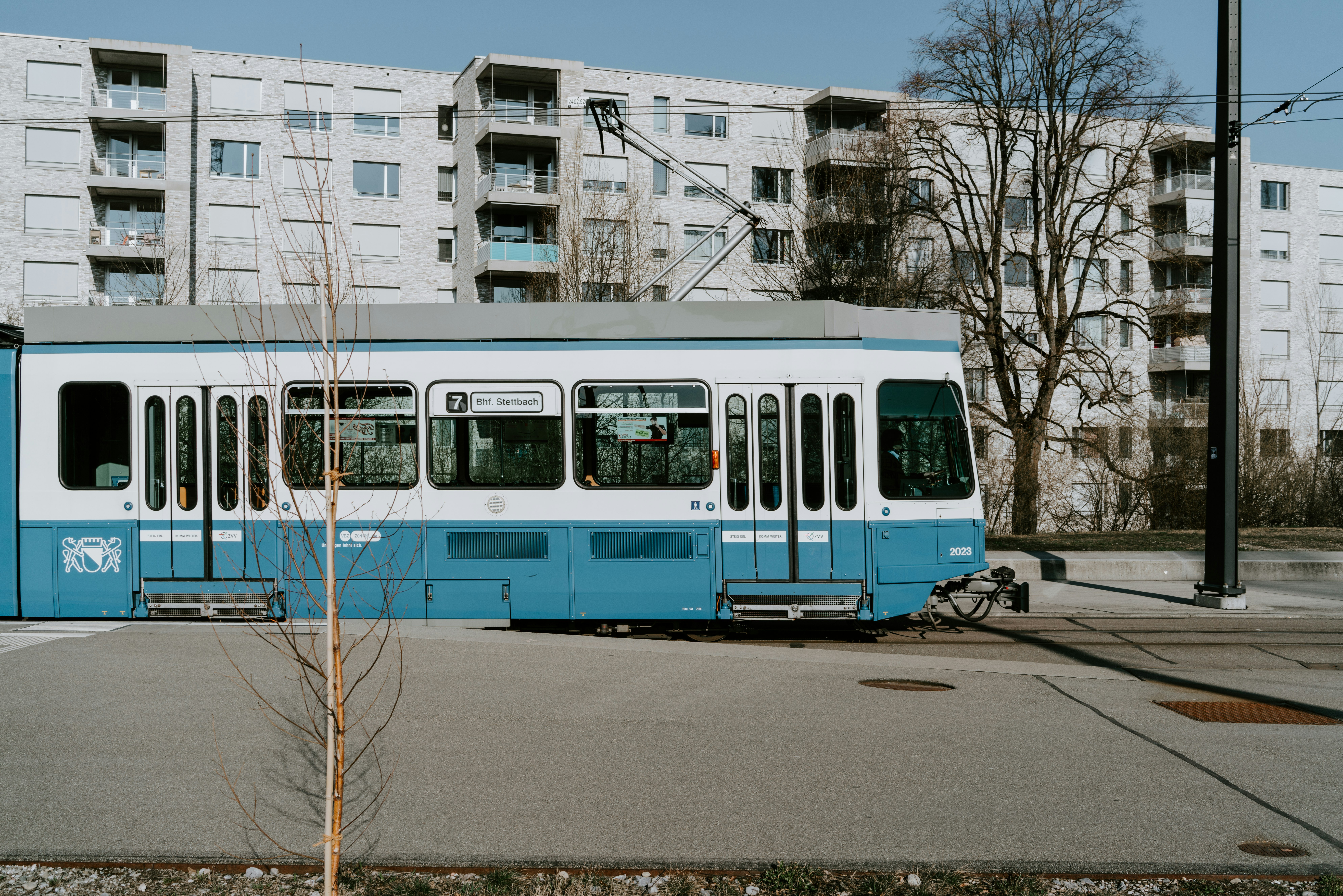 blue and white tram beside gray concrete multi-story building during daytime