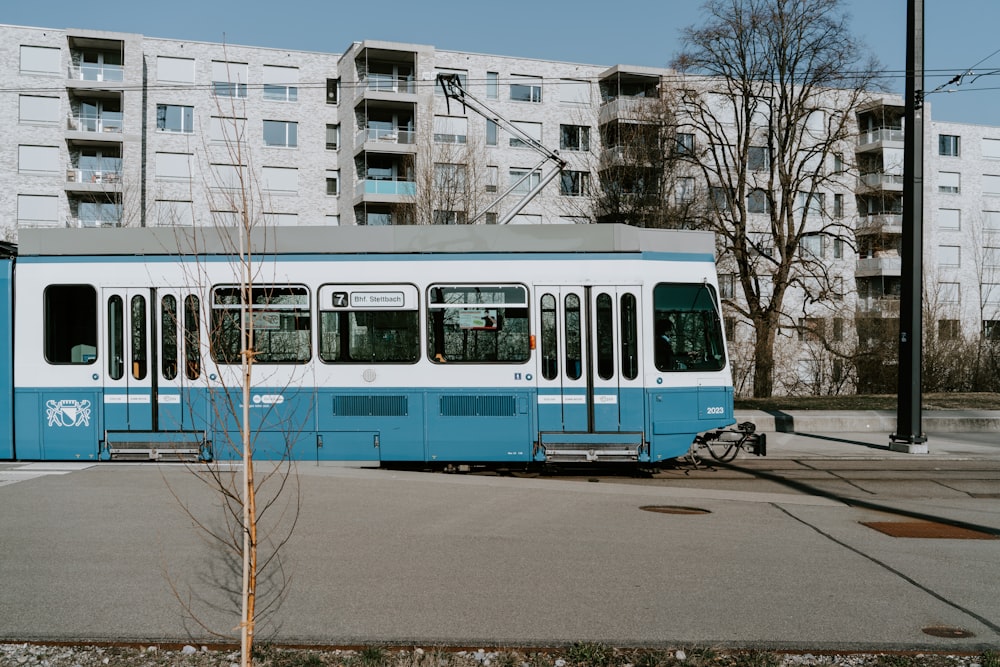 blue and white tram beside gray concrete multi-story building during daytime