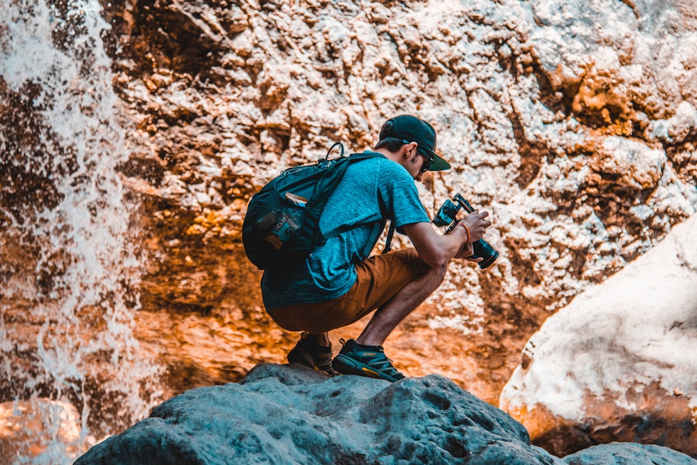 selective focus photography of man sitting on rock holding digital camera