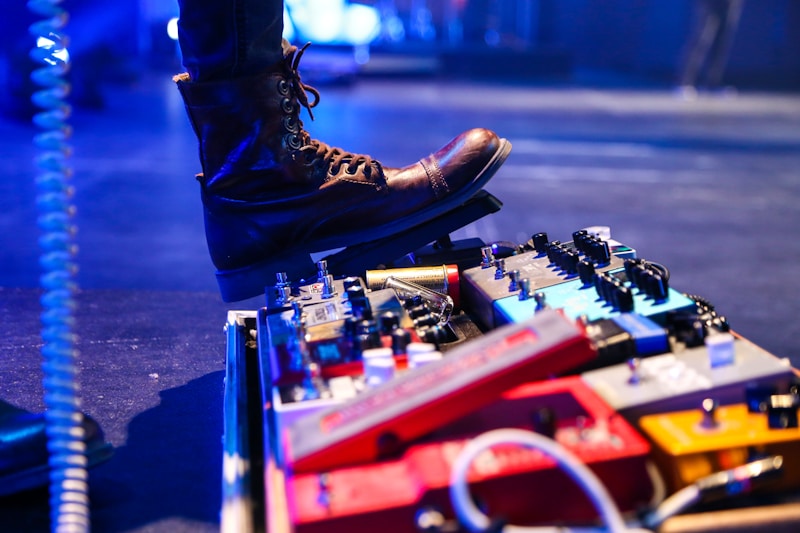 Worn boot on a pedalboard full of guitar pedals on a dark stage