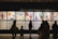 Silhouettes of people observing colorful and abstract artwork arranged in a gallery display. The artwork features various bold colors and dynamic shapes, with text panels below each visual piece.