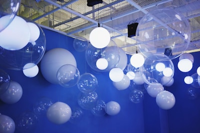 A ceiling decorated with a mix of white and transparent orbs in various sizes, suspended against a vibrant blue background. The orbs are illuminated, casting a soft glow, and contribute to a dreamy, whimsical atmosphere.