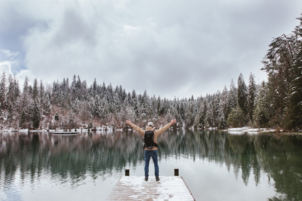 man standing on edge of dock near lake during daytime