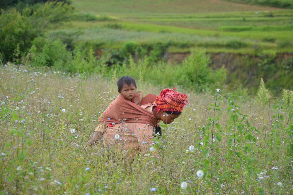 woman with baby wrap and baby on her back near plants during daytime