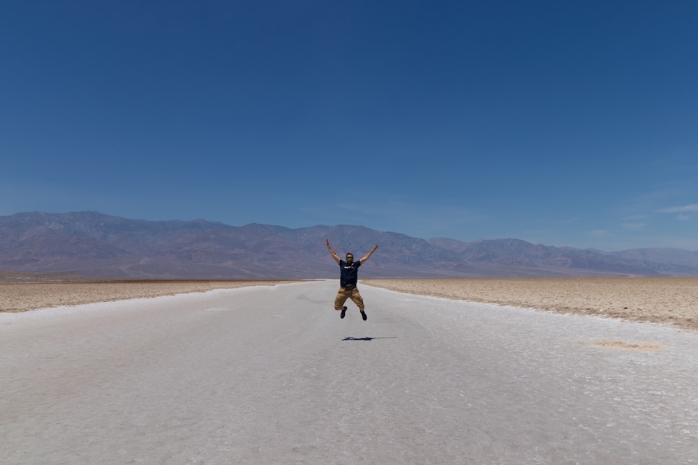 man jumping in middle of empty country road