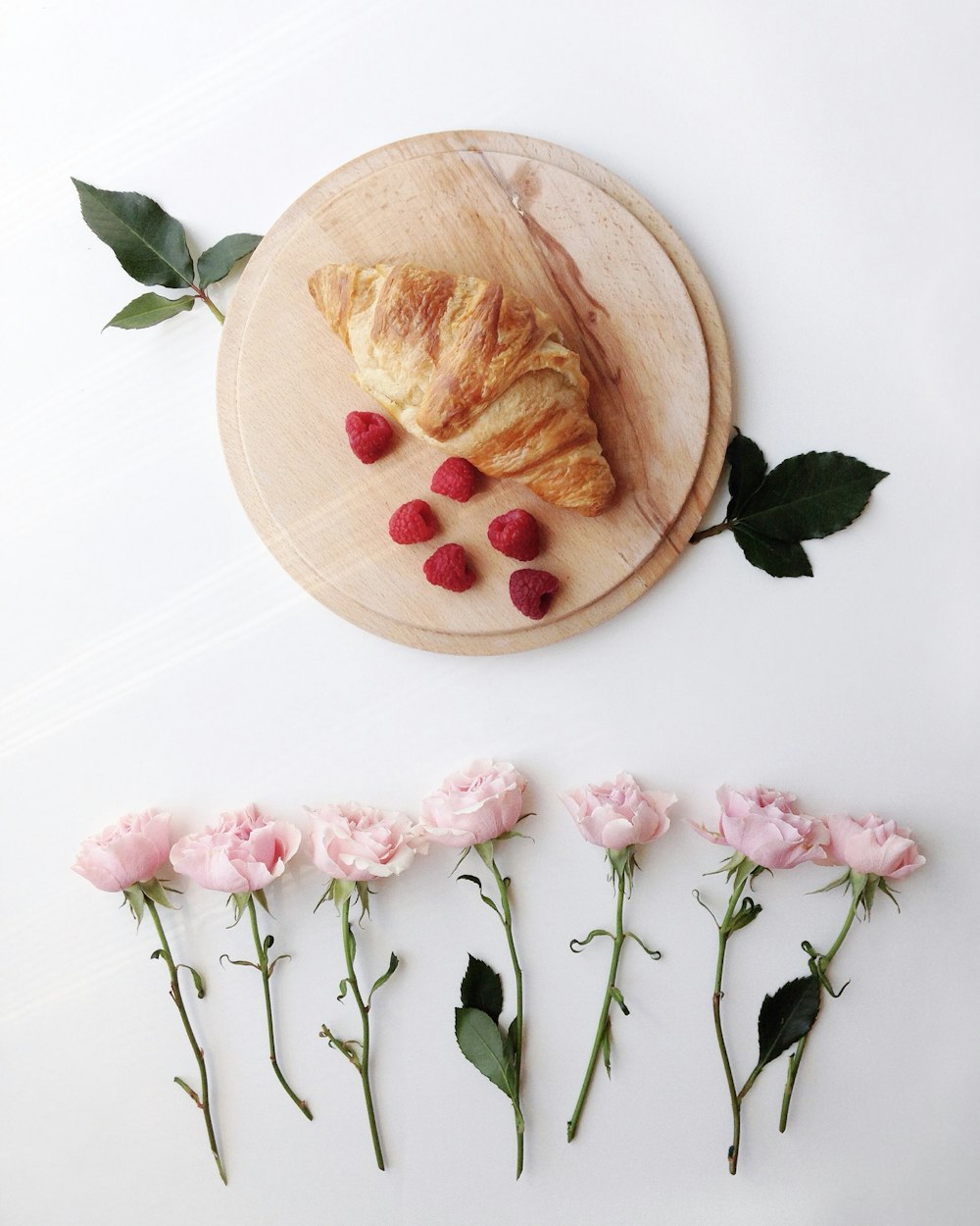 croissant and raspberries on round wooden tray