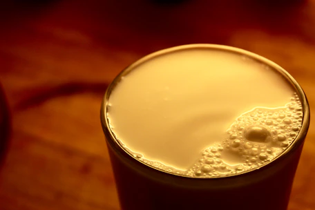 Close-up of creamy milk being poured into a glass in a bright, clean dairy facility.