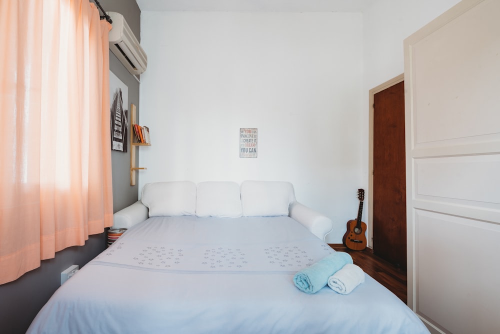 rolled blue and white towel on bed and ukulele near closed brown wooden door