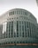 A large, modern office building with a curved facade and numerous windows. The building is labeled with the 'Thomson Reuters' logo. An electronic news ticker displays headlines along the bottom, contributing to the urban, corporate atmosphere.