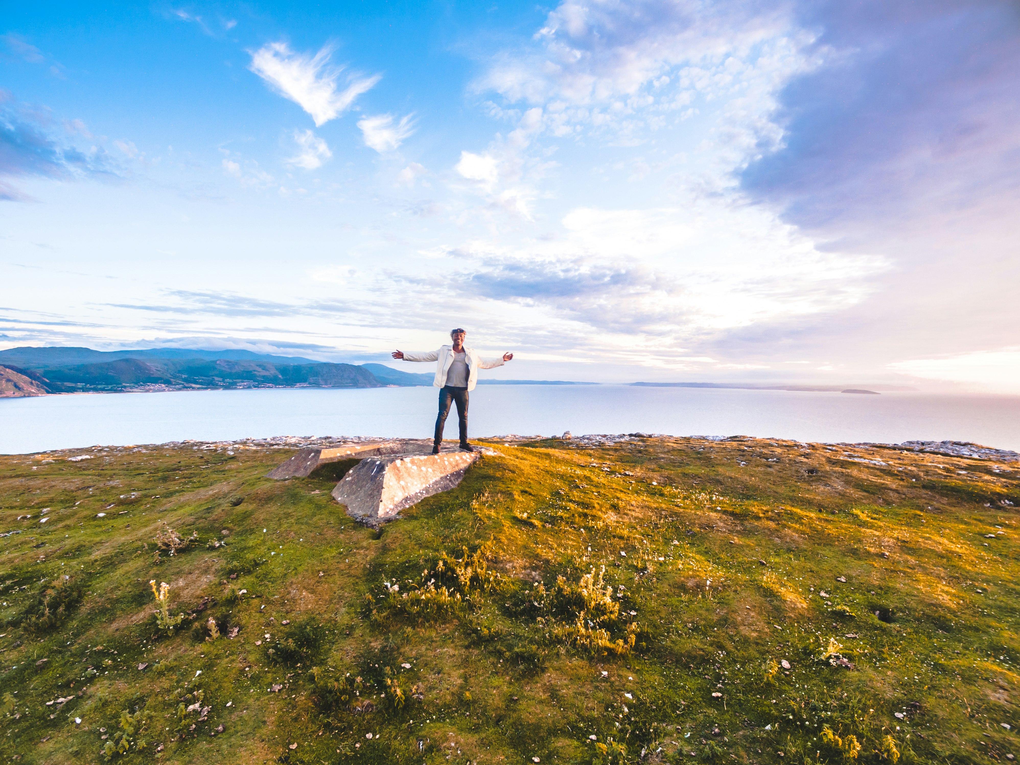 person in white top on brown rock beside green grass during daytime