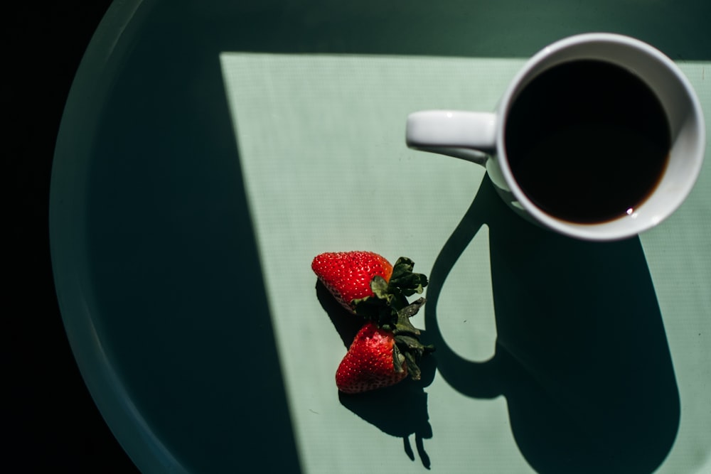 filled white mug beside two strawberries