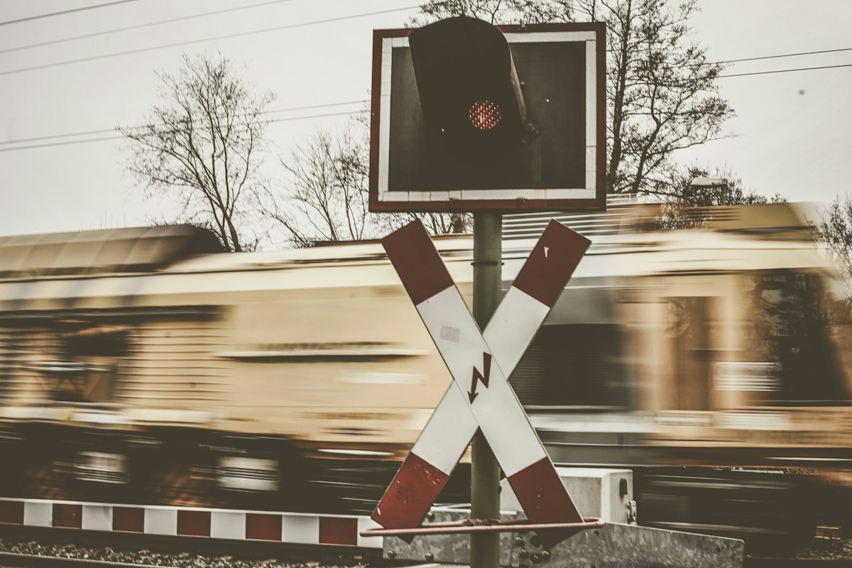 A railway crossing sign and a red signal light in sharp focus while a train rushes past in motion blur