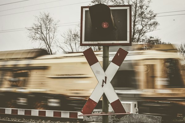 A railway crossing sign and a red signal light in sharp focus while a train rushes past in motion blur