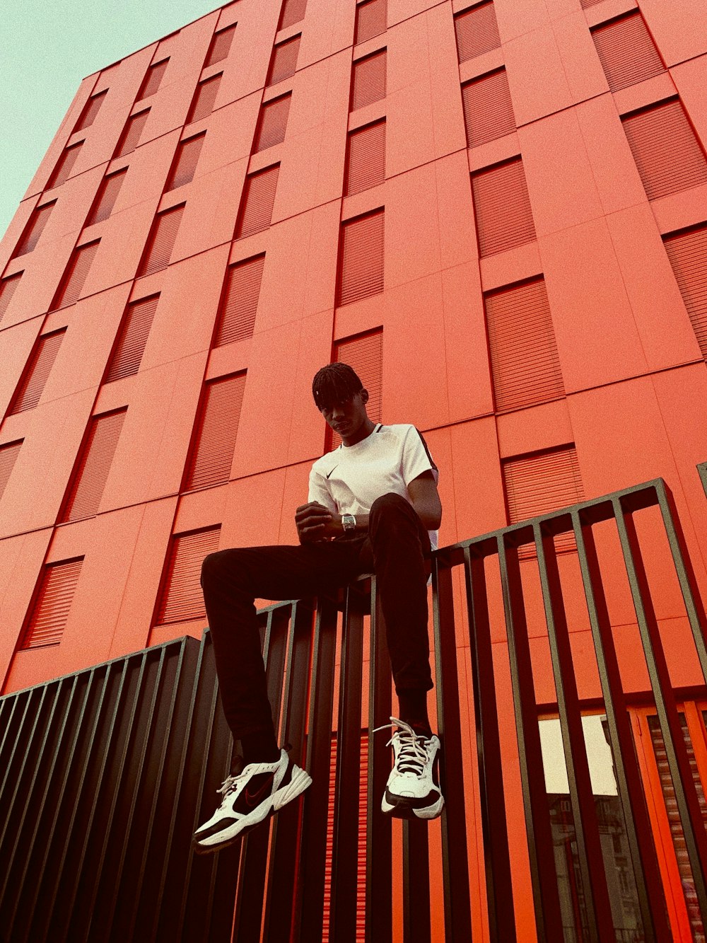 man sitting on black fence beside red concrete building