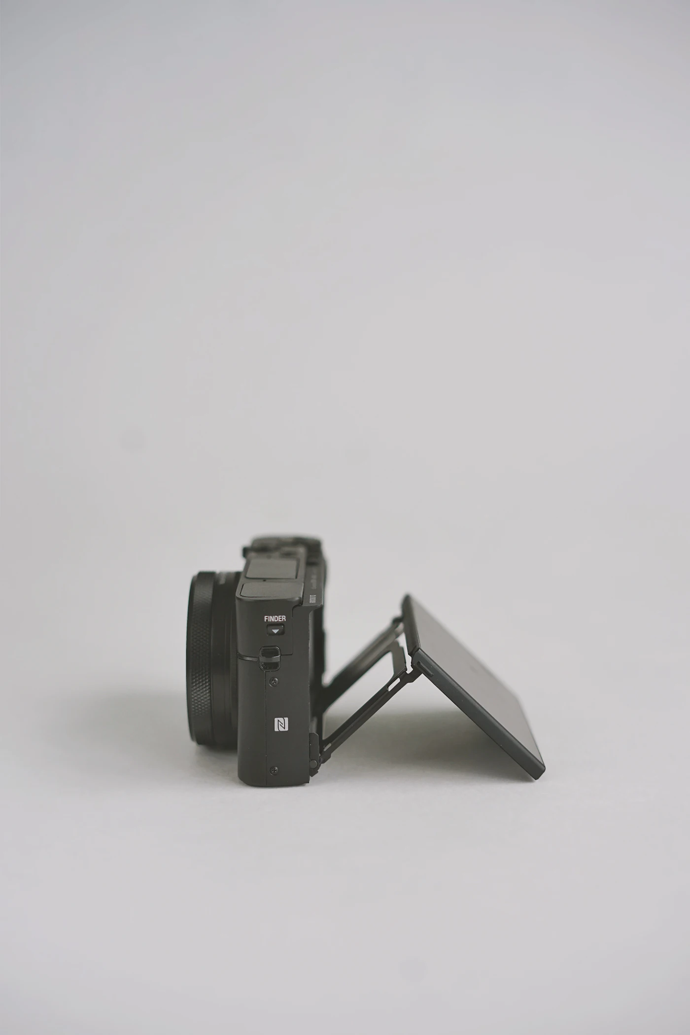 A small camera standing on a grey surface with its rear screen flipped out and tilted at an angle