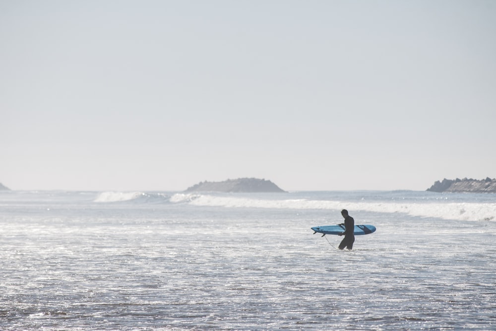 man holding blue surfboard while walking on beach