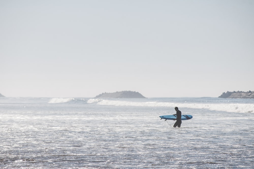 homme tenant une planche de surf bleue tout en marchant sur la plage