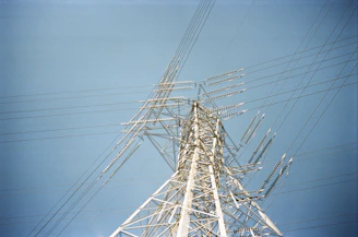 Construction workers assembling a high-voltage transmission tower against a clear blue sky.