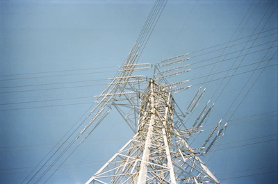 Construction workers assembling a high-voltage transmission tower against a clear blue sky.
