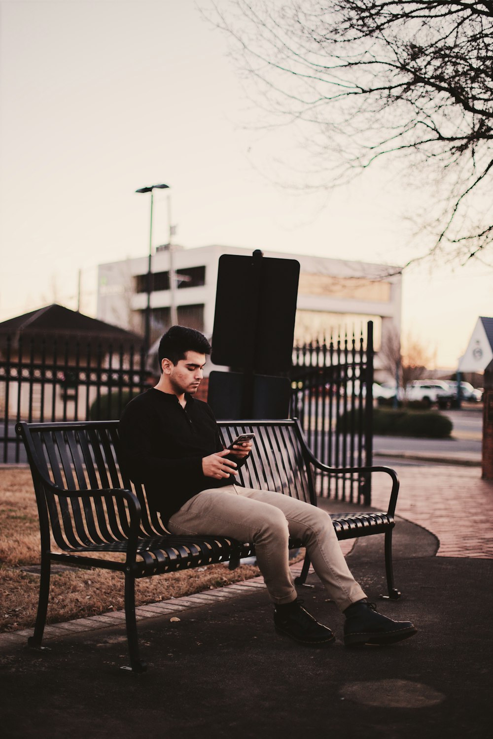 man sitting on black bench under withered tree