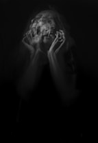 A black and white image capturing a blurred, emotional expression of a person with hands covering part of the face, creating a sense of movement and intensity.