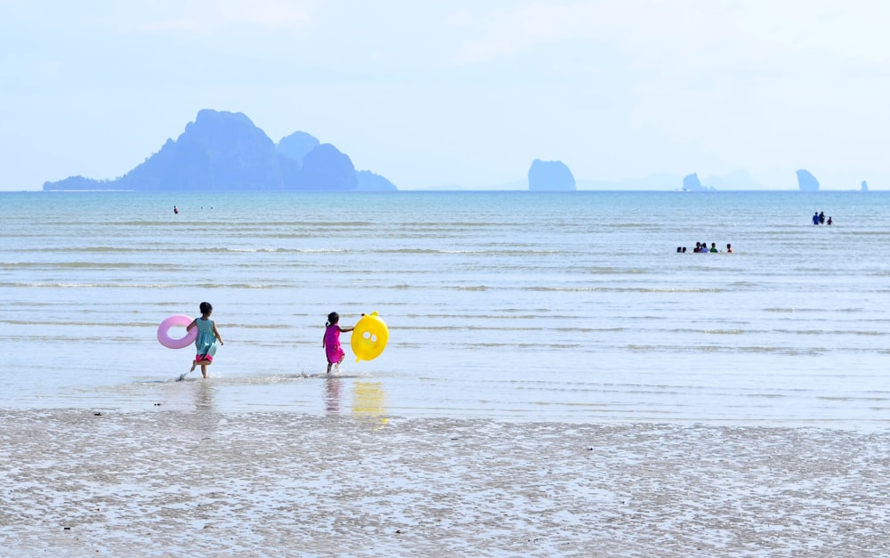 children's walking on seashore while holding inflatable bouy