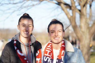 A man and woman outdoors, each wearing a Milana LLC scarf, smiling as the breeze catches the fabric gently.