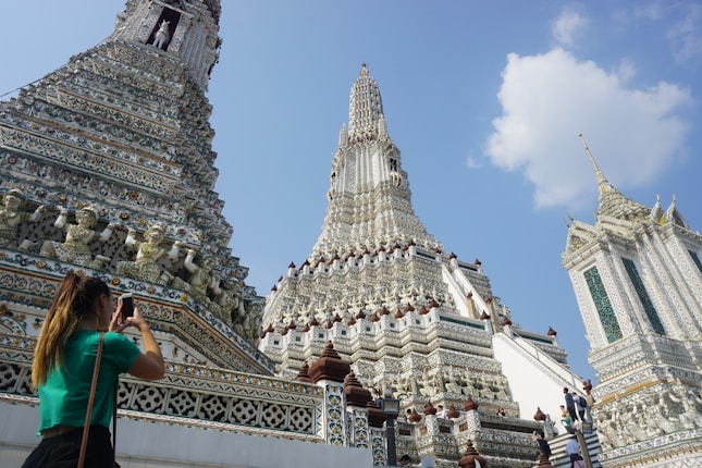 An intricately detailed temple with ornate carvings and patterns on its towers, highlighting its architectural beauty under a clear blue sky. A person is capturing the scene with a camera, indicating awe and admiration for the structure.
