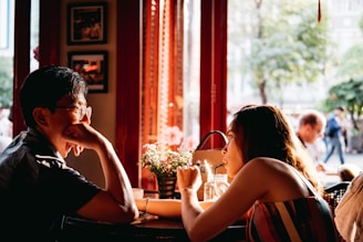 man wearing black collared top sitting on chair in front of table and woman wearing multicolored top