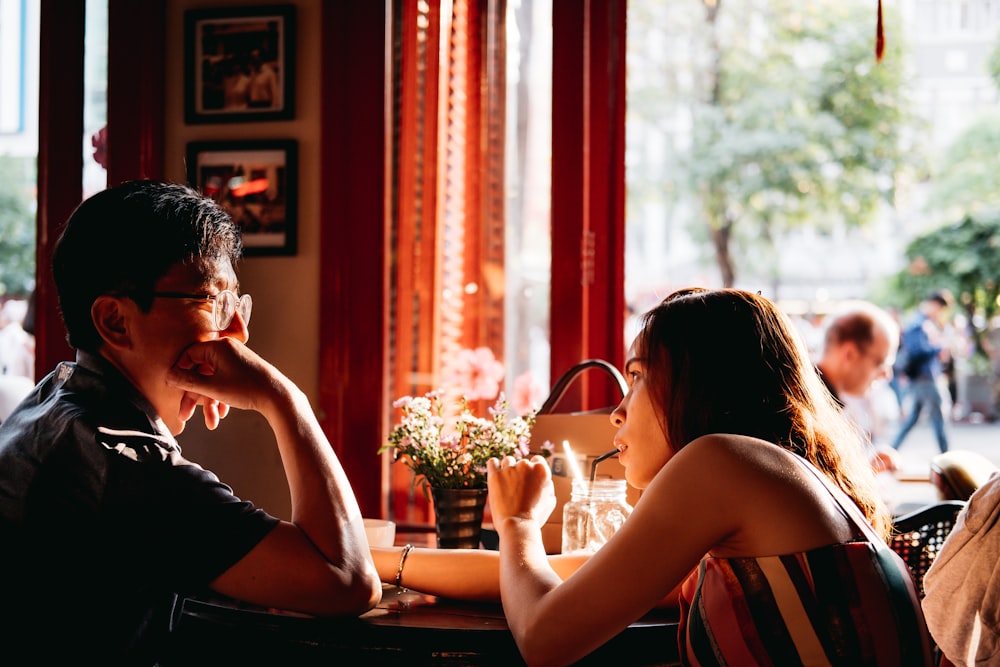 man wearing black collared top sitting on chair in front of table and woman wearing multicolored top