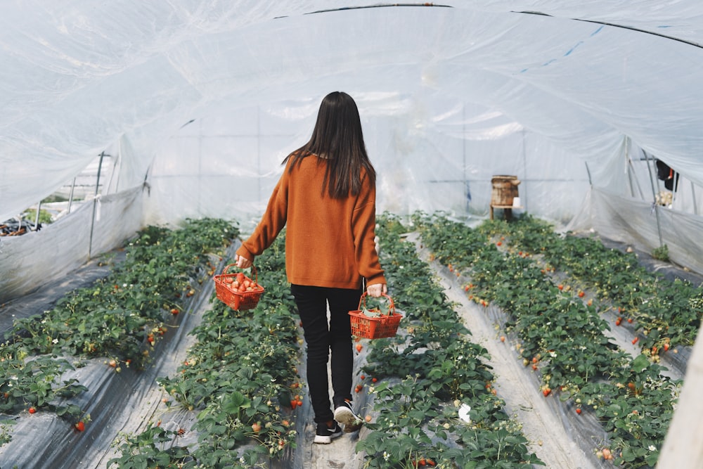 woman in brown sweater holding two baskets while walking on green house